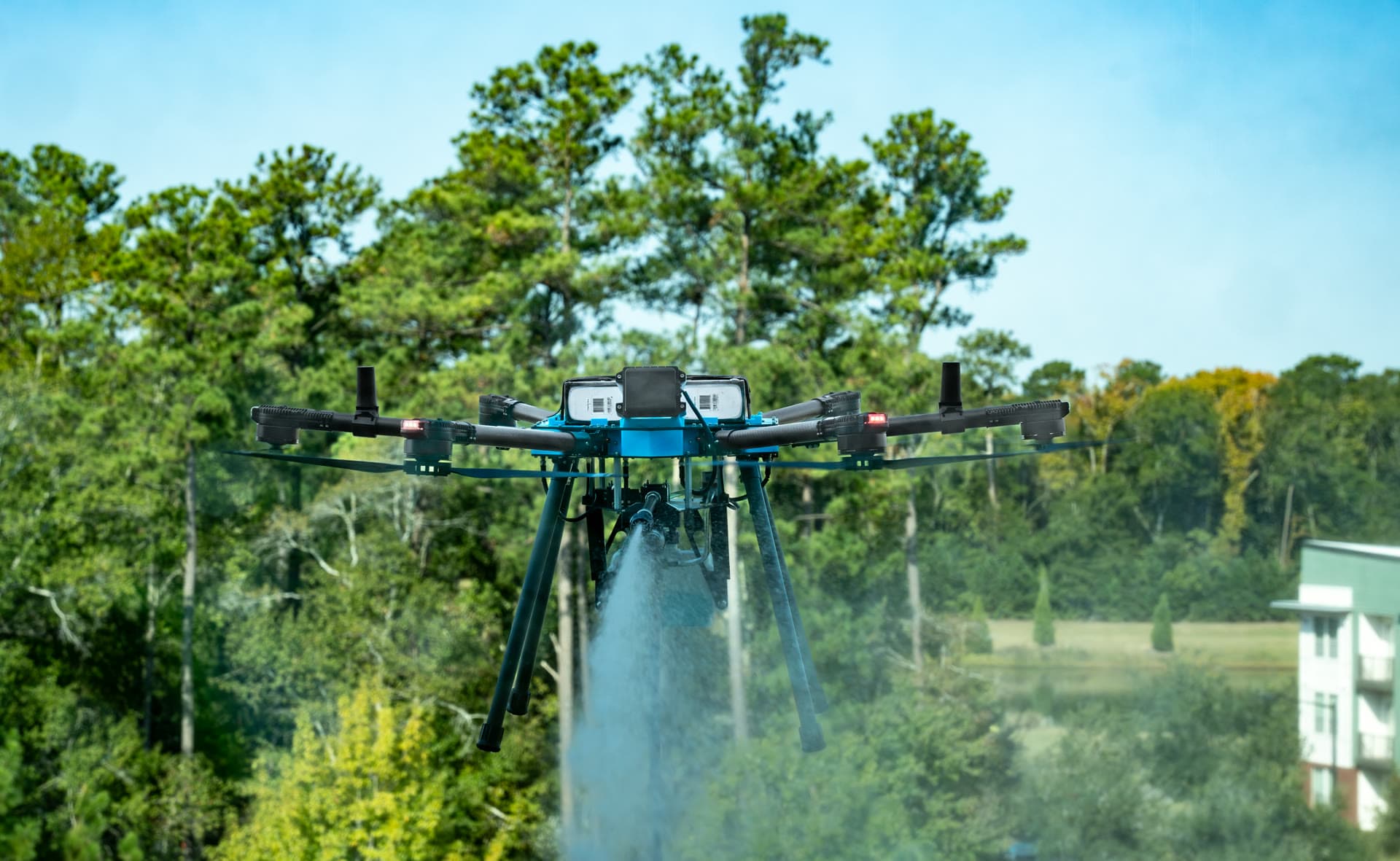 Drone spraying cleaning solution with trees and buildings in background